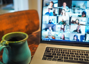 laptop showing video call with lots of people on it ang a mug