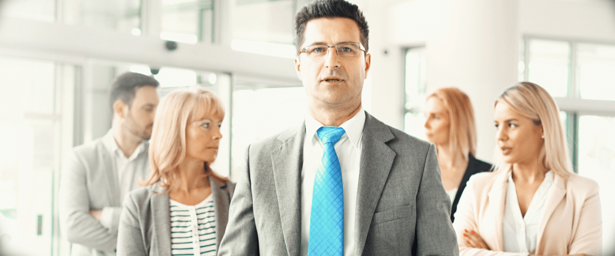 man in suit with four people in office attire behind him to illustrate article regarding agency conflicts