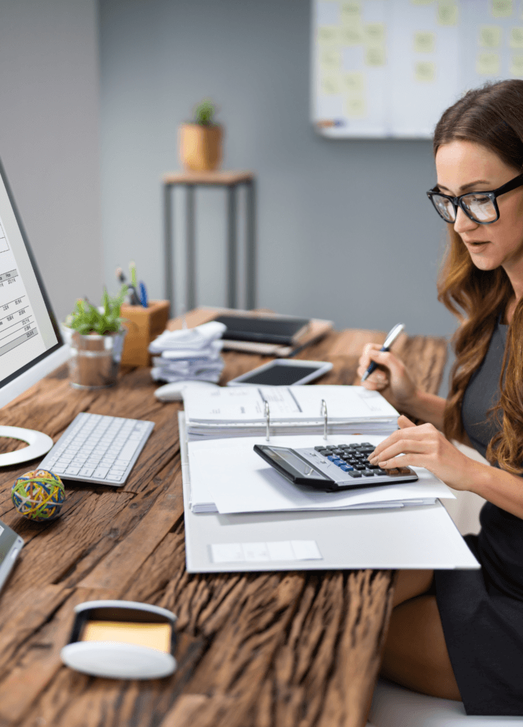 Young woman in glasses at a desk with a computer, folder and calculator, used to illustrate the idea of reviewing business size for IR35.